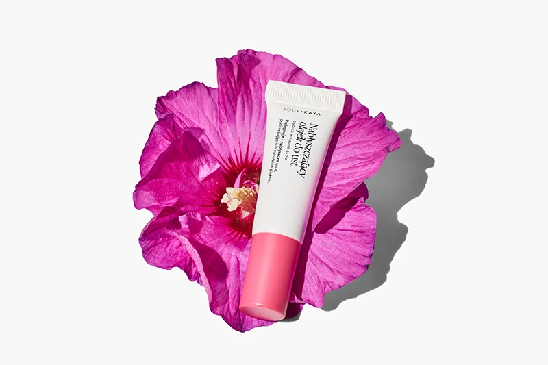 Kreatywna fotografia kosmetyków w Warszawie - stylizowany flat lay olejku do ust na różowym kwiecie hibiskusa, wykonany przez Packshothouse.